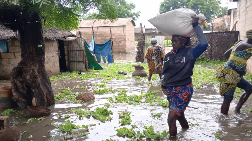 A women moving through a flooded village with the harvest she could rescue from the water. Photo: Samuel Sawalda/UNFPA Cameroon, 2024. 